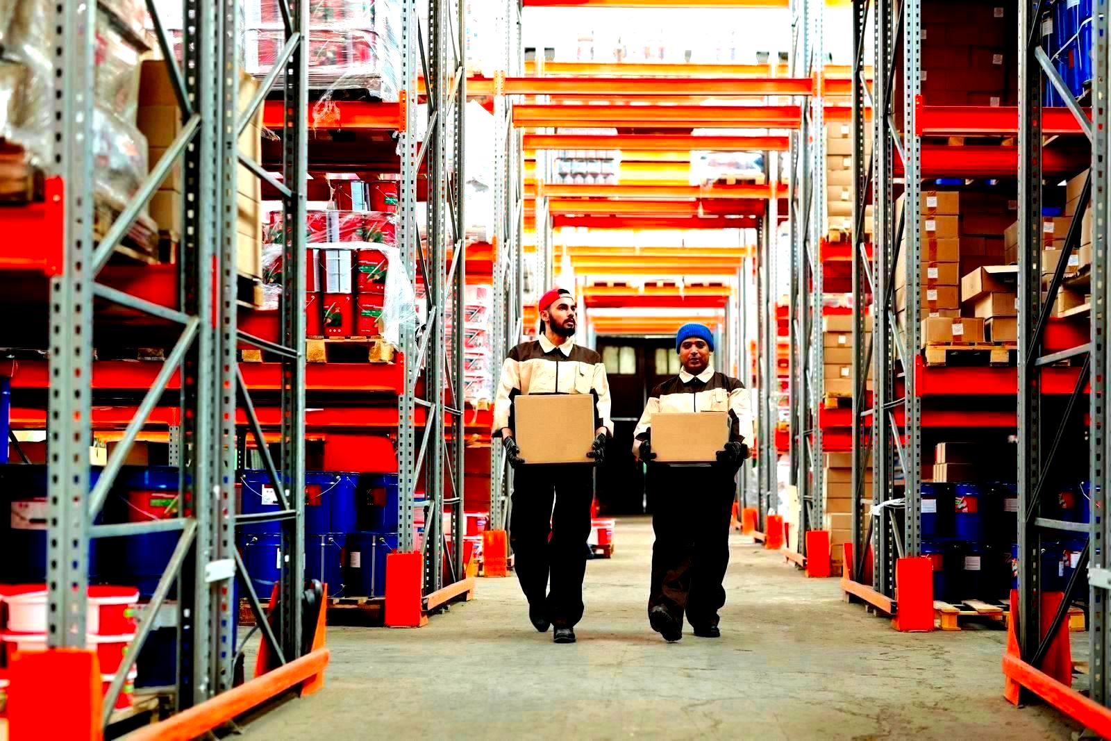 Two workers carrying parcels between shelves in a warehouse