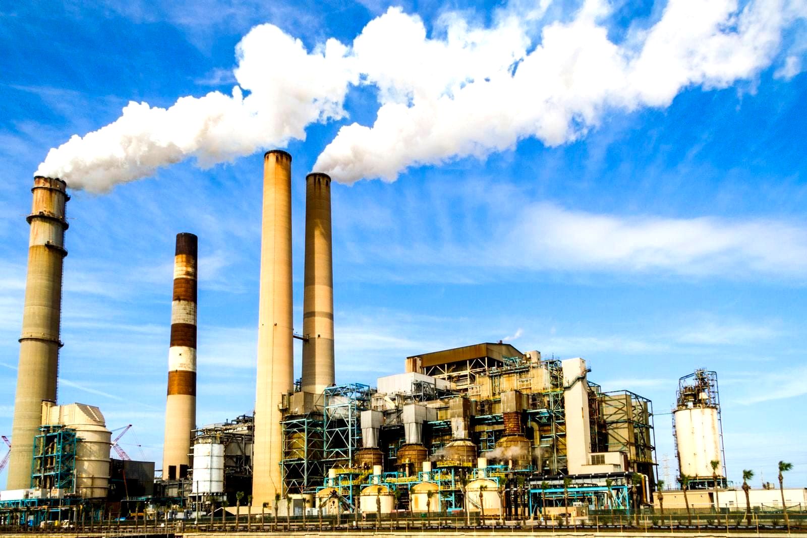 Industrial factory with smokestacks emitting white steam against a gray sky