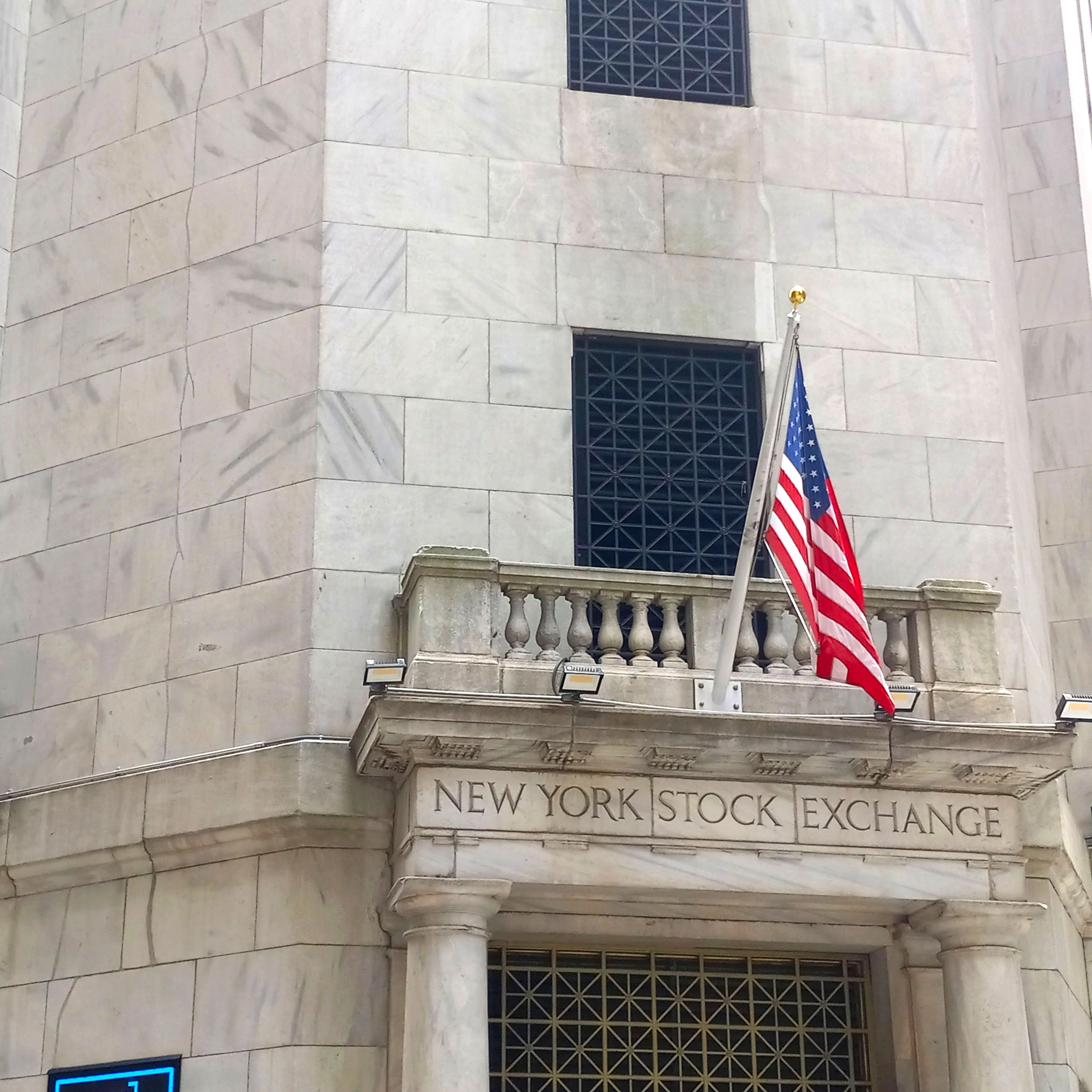 New York Stock Exchange building exterior on Wall Street with American flags