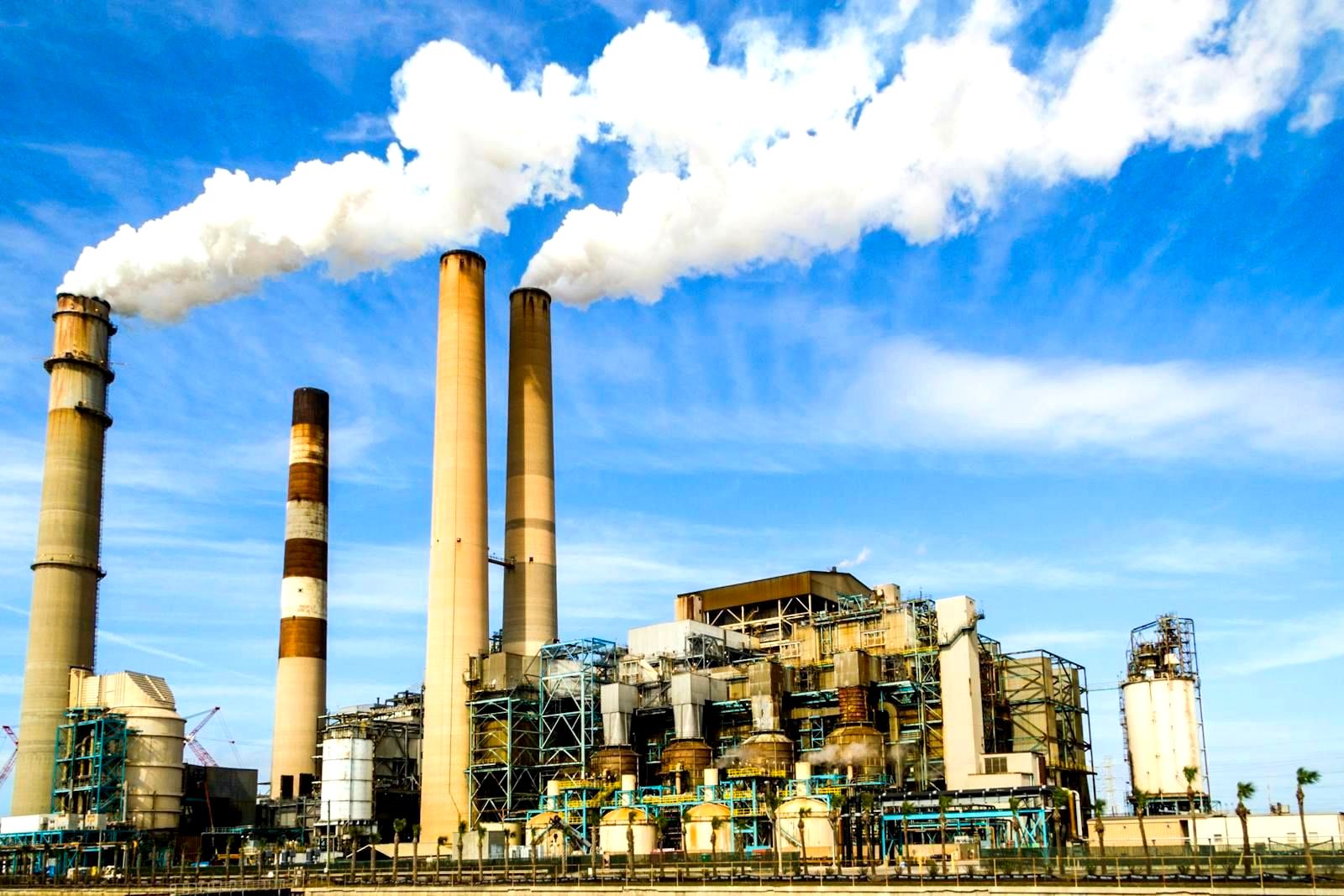 Industrial smokestacks against a blue sky with white smoke